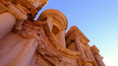 Looking-up-at-The-Monastery-Ed-Deir-building-carved-into-mountains-against-blue-sky-in-the-ancient-city-of-Petra-in-Jordan