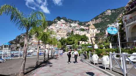 People-Walking-on-the-Promenade-of-Positano-Beach-Surrounded-by-Tall-Mountains-and-Beautiful-Coastal-Homes,-Amalfi-Coast,-Italy