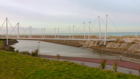 Modern-pedestrian-bridge-over-a-serene-river-leading-to-the-sea-in-Dunkerque,-France