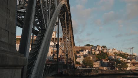 Dom-Luís-I-Bridge-side-view-at-sunset-with-historic-hillside-buildings-in-Porto,-Portugal