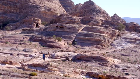 Tourist-walking-over-rugged-rocky-mountainous-terrain-of-red-sandstone-within-the-City-of-Petra-in-Jordan