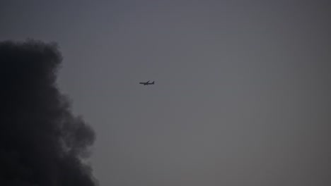 An-aeroplane-flying-and-vanishing-into-the-dark-smoke-from-a-fire