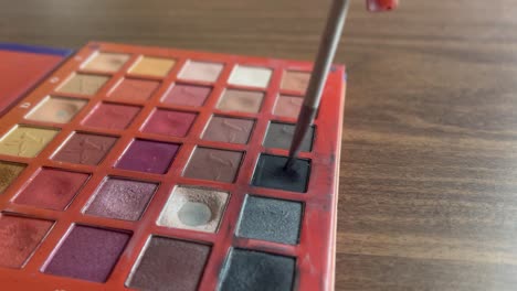 Brush-picking-black-paint-from-a-vibrant-facepaint-palette-on-a-wooden-table-close-up