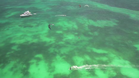 Kite-surfers-and-a-yacht-on-clear-turquoise-waters,-aerial-view