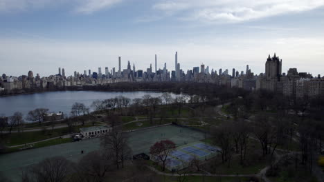 Central-Park-leisure-courts-and-The-Lake,-aerial-view,-sunny-Manhattan-skyline-in-background-during-bright-summer-day,-New-York-City