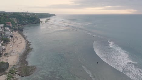 High-Angle-Drone-of-Bingin-Beach,-Bali,-Uluwatu-Indonesia-at-golden-hour-sunset-with-low-tide-reef-and-surfers