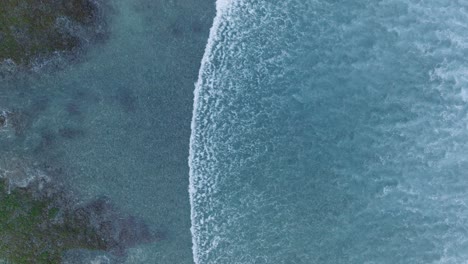 Top-Down-Slow-Motion-Drone-of-wave-action-at-low-tide-over-coral-and-rock-reef-Nyang-Nyang-Beach,-Bali,-Uluwatu-Indonesia