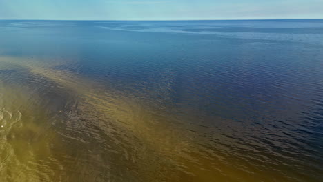 Aerial-drone-top-down-shot-over-delicate-ripples-on-the-surface-of-sea-water-with-reflection-of-sunlight-falling-on-it-on-a-sunny-day