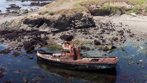 Aerial-reverse-pullback-panning-shot-of-a-fishing-boat-shipwreck-beached-on-the-coast-in-Cayucos,-California