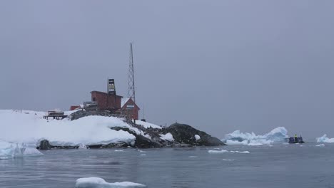 Buildings-on-Coast-of-Antarctica-and-People-Sailing-in-Boat-Between-Icebergs,-Slow-Motion