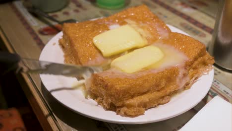 A-customer-cuts-in-half-a-ready-to-eat-Hong-Kong-style-French-toast-consisting-of-deep-fried-bread,-peanut-butter,-butter,-and-condensed-milk-at-a-restaurant