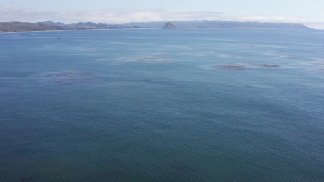 Low-aerial-shot-tilting-up-to-Morro-Rock-in-the-distance-from-Cayucos,-California