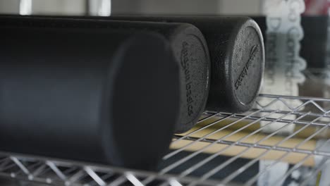 The-view-showcases-a-pair-of-black-foam-rollers-situated-on-a-shelf,-designed-for-exercise-and-yoga-purposes