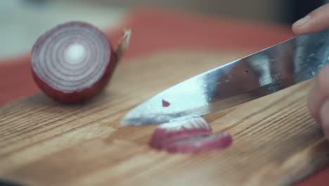 A-close-up-shot-of-a-man-cutting-onion-to-slices-on-a-wooden-board,-4K-video