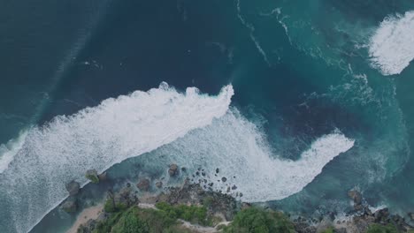 Top-Down-Drone-of-unidentifiable-surfers-at-sunset-with-deep-blue-and-gold-water-and-coastline-at-Padang-Padang,-Bali,-Uluwatu-Indonesia