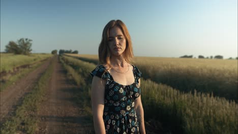 Young-woman-on-dirt-road-enjoying-the-calm,-peaceful-and-serene-summer-sunset-with-light-shining-on-her-hair-during-golden-hour-in-cinematic-slow-motion