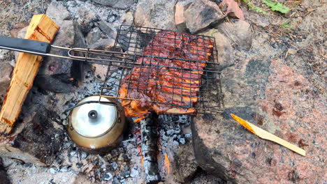 Tasty-meat-ribs-grilling-on-a-campfire-under-fire-with-a-wooden-fork,-closing-in