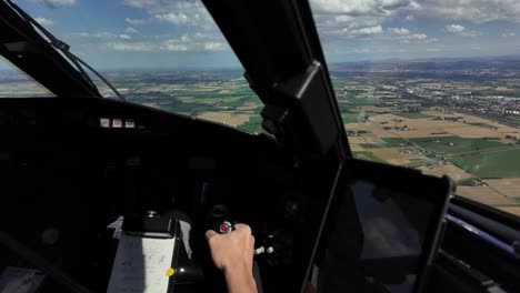 Hand-of-a-white-pilot-piloting-the-flight-wheel-in-a-real-time-flight-over-some-brown-and-green-fields-at-low-altitude