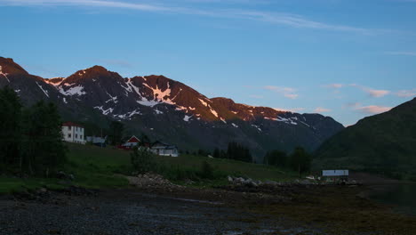 Timelapse-of-a-Norwegian-farm-in-front-of-pointed-mountains-bathed-in-midnight-sun,-Lofoten-Islands,-Norway