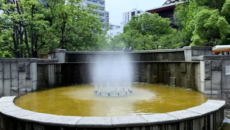 Fountain-in-a-peaceful-urban-park-surrounded-by-trees-and-buildings-on-a-clear-day