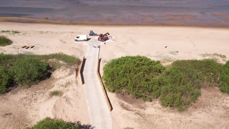 Aerial-view-of-repair-works-along-the-Baltic-Sea-coast,-featuring-visible-construction-machinery-and-a-concrete-footbridge