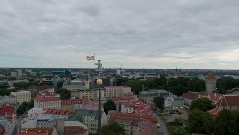 Eine-Drohnenaufnahme-Des-Alten-Thomas-Auf-Einem-Gebäude-In-Tallinn,-Estland,-Der-Eine-Goldene-Flagge-Hält