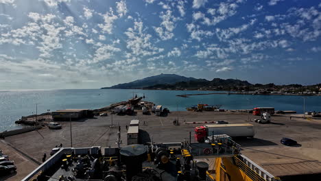 Busy-port-of-Zakynthos-with-trucks,-equipment,-and-a-scenic-mountain-backdrop-on-a-sunny-day