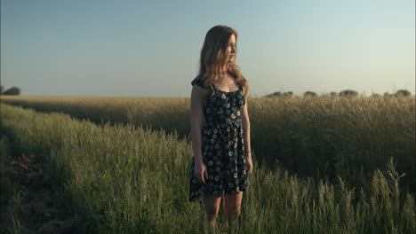 Young-woman-in-meadow-on-farm-enjoying-the-calm,-peaceful-and-serene-summer-sunset-with-light-shining-on-her-hair-during-golden-hour-in-cinematic-slow-motion