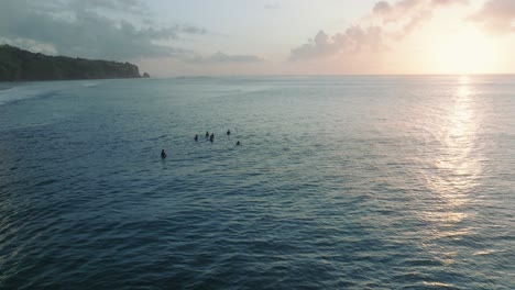 Slow-Motion-Drone-of-unidentifiable-surfers-waiting-for-waves-at-sunset-with-deep-blue-and-gold-water-at-Padang-Padang,-Bali,-Uluwatu-Indonesia