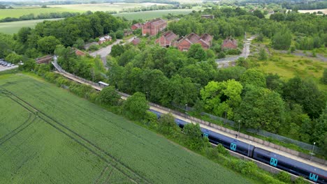 Blauer-Südostzug-Fährt-Langsam-In-Einen-Dorfbahnhof-Auf-Dem-Land-Ein,-Im-Hintergrund-Einige-Verlassene-Gebäude