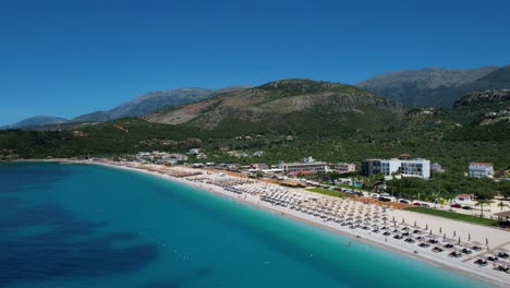 Vibrant-Coastal-Colors-of-Albanian-Riviera-with-Blue-Ionian-Sea,-White-Sandy-Beach,-Green-Hills,-and-Clean-Hotels-and-Resorts