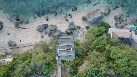 Drone-Descendente-De-Arriba-Hacia-Abajo-De-La-Costa-Con-Escalera-Y-Arrecife-De-Coral-En-La-Playa-De-Bingin,-Bali,-Uluwatu-Indonesia-Al-Atardecer-De-La-Hora-Dorada