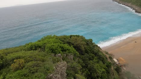 Drone-footage-capturing-a-descent-from-mountains-to-Gjipe-Beach,-revealing-lush-greenery-and-the-pristine-blue-sea-along-the-Albanian-coastline