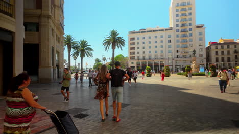 People-walking-in-a-busy-plaza-lined-with-palm-trees-and-surrounded-by-classic-buildings-in-Malaga