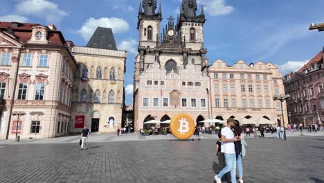 Zwei-Männer-Tragen-Eine-Riesige-Bitcoin-Münze-Durch-Die-Innenstadt-Von-Prag