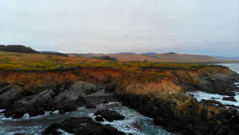 Rugged-Central-California-Cliffs-drone-fly-in-to-San-Simeon-coastline-with-Pacific-Ocean-crashing-waves,-Hearst-Castle-in-distance,-4k-Pro-Res-422-HQ