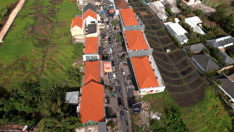 Aerial-view-of-a-congested-street-lined-with-buildings-with-orange-roofs-in-Canggu,-surrounded-by-green-fields-and-residential-areas