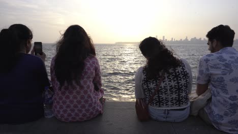 Young-couple-sitting-at-Marin-Drive-beach-overlooking-Mumbai-skyline-buildings-in-the-evening-at-sunset