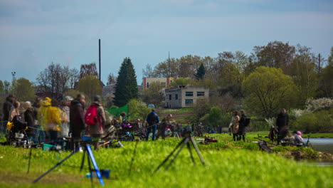 Many-fishermen-on-river-coast-on-sunny-day-in-Latvia-fish-festival,-time-lapse-view