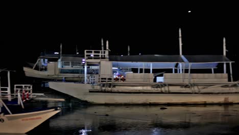 Touring-boats-are-parked-for-the-night-at-a-pier-near-the-promenade-area-of-a-seaside-restaurant