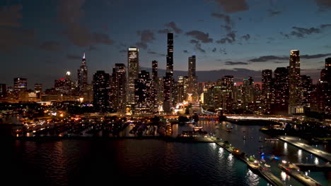 Aerial-view-approaching-the-illuminated-lakefront-of-Chicago,-summer-dusk-in-USA