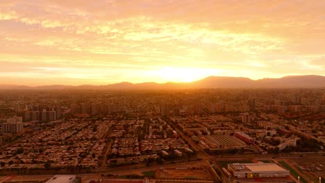 Aerial-panoramic-view-of-a-Santiago-city-during-sunset-with-the-sun-casting-a-warm-glow-over-buildings-and-distant-mountains-Pull-Back-shot