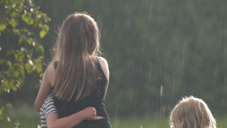 Niños-Felices-Abrazándose-En-El-Jardín-Mientras-Llueve