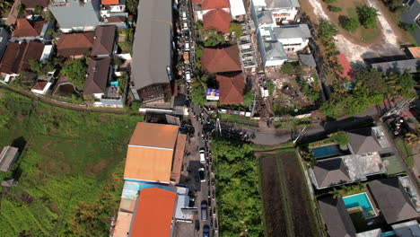 A-bustling,-narrow-street-in-Canggu,-teeming-with-traffic-and-bordered-by-a-mix-of-modern-and-traditional-buildings,-lush-greenery,-and-residential-homes