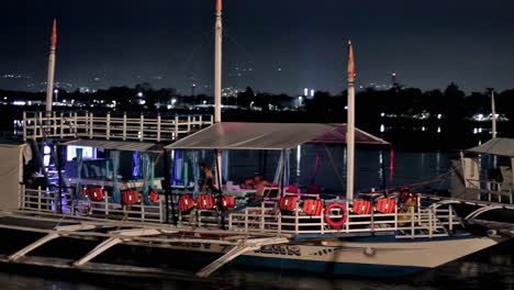 Los-Barcos-Turísticos-Están-Estacionados-Para-Pasar-La-Noche-Cerca-De-Un-Muelle-Cerca-Del-Paseo-Marítimo-De-Un-Restaurante-Junto-Al-Mar