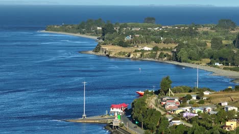 Luftaufnahme-Eines-Ruhigen-Chacao-Küstendorfes-Mit-Blauem-Wasser-Und-Verstreuten-Häusern-Entlang-Der-Küste