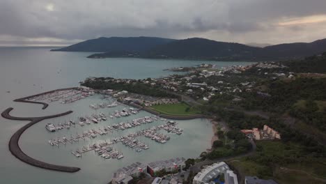 Port-Airlie-Beach-Bay-Lagoon-Coral-Sea-marina-aerial-drone-dark-rain-clouds-mist-sunrise-morning-heart-of-Great-Barrier-Reef-Whitsundays-Whitehaven-jetty-yachts-sailboats-buildings-circle-left-motion