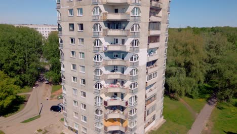 Drone-footage-descending-over-a-concrete-layered-USSR-apartment-block-surrounded-by-greenery