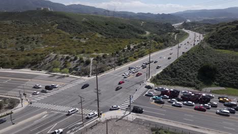 Aerial-view-of-cars-driving-through-intersection-between-green-fields-and-mountains