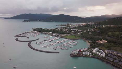Port-Airlie-Beach-Bay-Lagoon-Coral-Sea-marina-aerial-drone-rain-clouds-mist-sunrise-morning-heart-of-Great-Barrier-Reef-Whitsundays-Whitehaven-jetty-yachts-sailboats-buildings-circle-to-the-left
